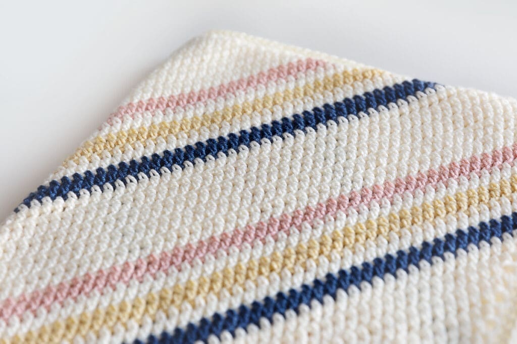 Corner to Corner Crochet Baby Blanket with Strips on White Surface